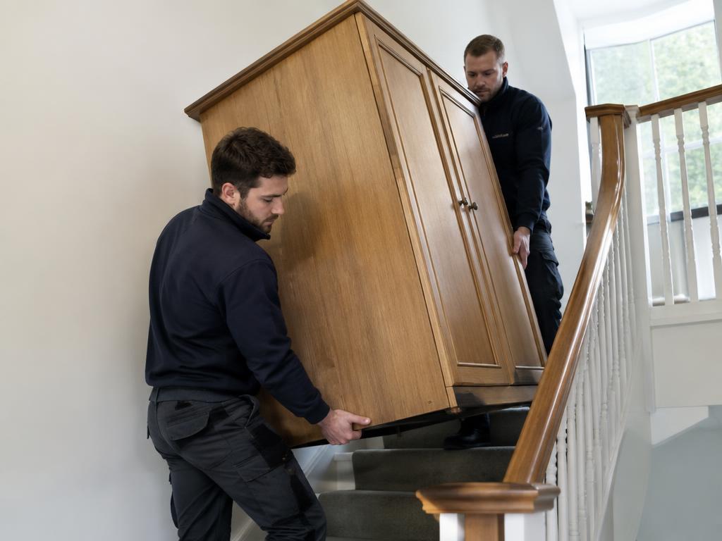 Zwei Mitarbeiter tragen einen Schrank durchs Treppenhaus